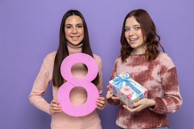 Due ragazze sorridenti nella felice festa della donna che tengono il numero otto con un regalo