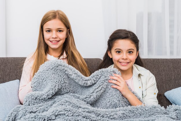 灰色の毛布で覆っているソファーに座っていた2人の女の子の笑顔