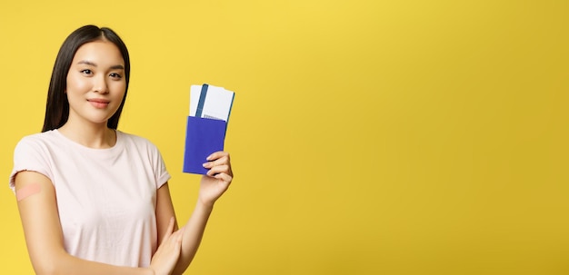 Foto gratuita sorridente vaccinato da una ragazza asiatica covida che mostra il passaporto con i biglietti per ottenere il vaccino contro il coronavirus