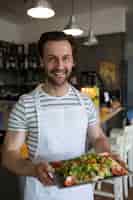 Foto gratuita sorridente cameriere con un vassoio di insalata in ristorante
