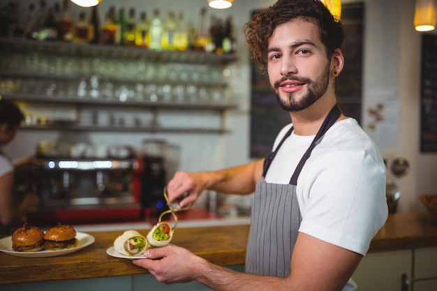 Smiling waiter holding a plate of vegetable roll in cafÃ©