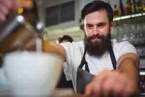 Free photo smiling waiter making cup of coffee at counter