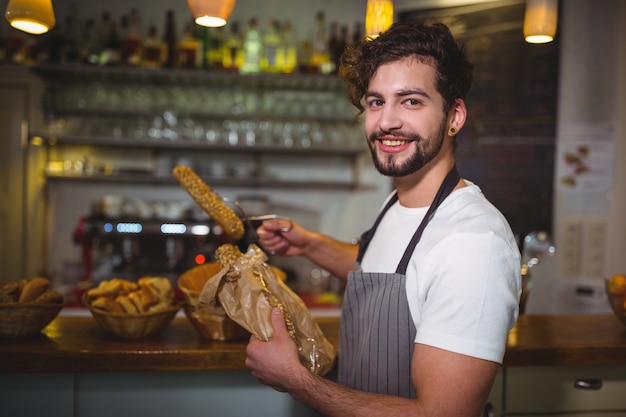 Smiling waiter packing croissants in paper bag at cafÃ©