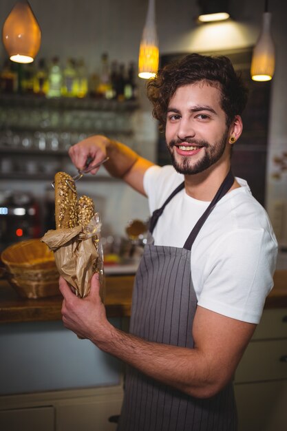 Smiling waiter packing croissants in paper bag at cafÃ©