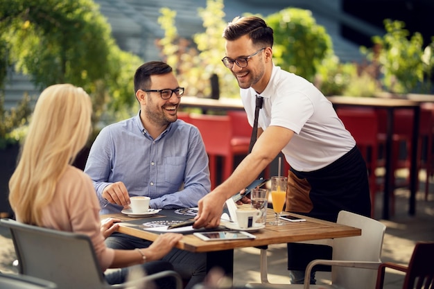 Smiling waiter serving guests in a restaurant and preparing their table for dining