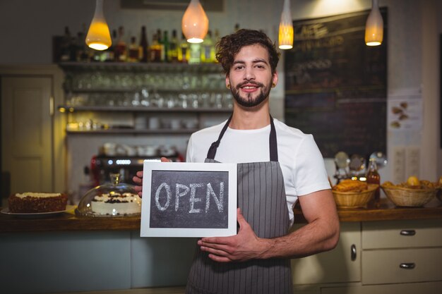 Smiling waiter showing slate with open sign in cafÃ©