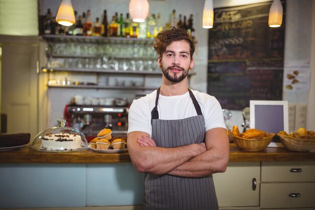 Smiling waiter standing with arms crossed in cafÃ©