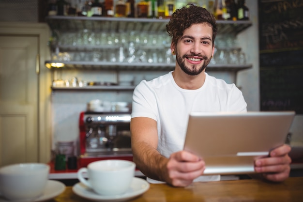 Smiling waiter using digital tablet at counter in cafÃ©