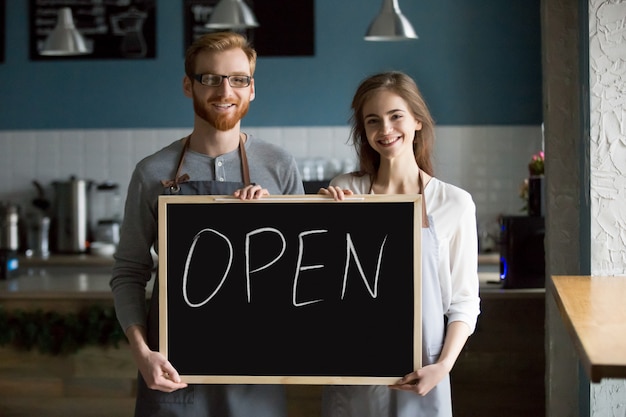 Smiling waiter and waitress holding chalkboard with open sign, portrait