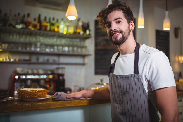 Smiling waiter wiping counter with napkin in cafÃ©