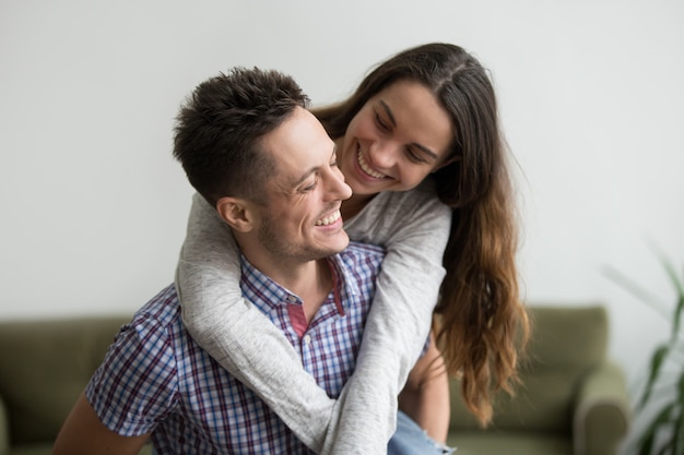 Smiling wife laughing embracing young husband piggybacking her at home