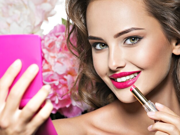 Smiling Woman applying lipstick. Beautiful girl makes makeup