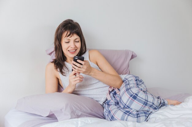 Smiling woman in bed typing on smartphone