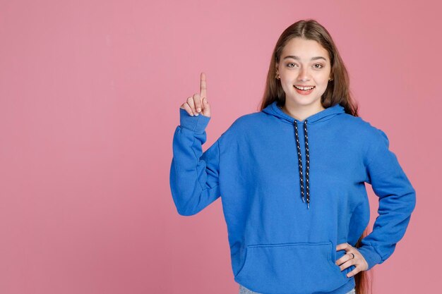 Smiling woman in bright blue pullover raising forefinger up while having fresh idea indoors