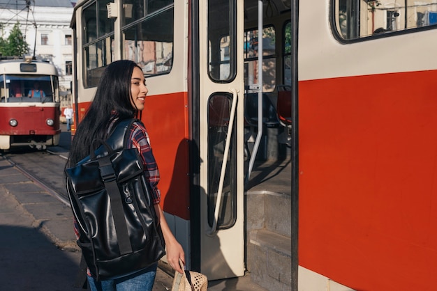 Smiling woman carrying backpack and holding hat standing in front of tramp door