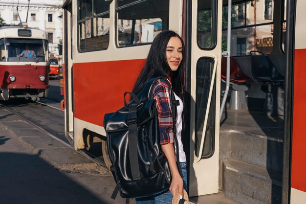 路上の路面電車の近くに立ってバックパックを運ぶ笑顔の女性