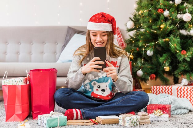 Smiling woman in Christmas hat messaging on floor 