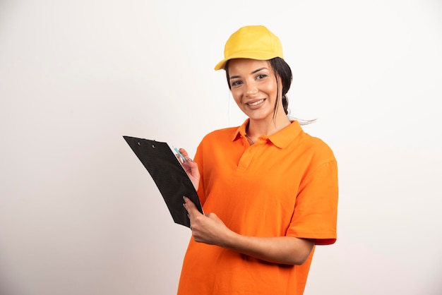 Smiling woman courier holding clipboard on white wall.