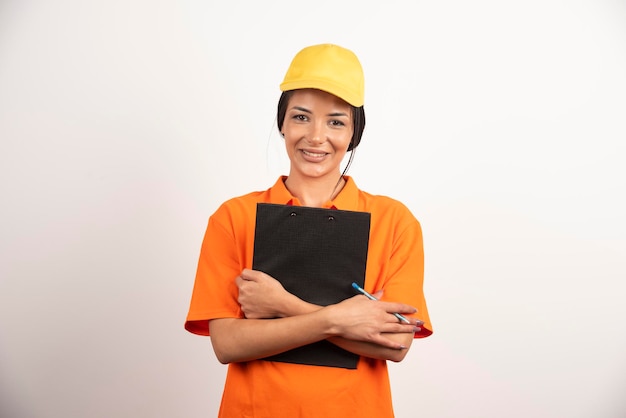 Smiling woman courier holding clipboard on white wall.
