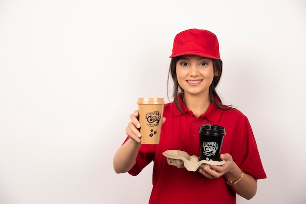 Smiling woman courier holding coffee for delivery on white background.