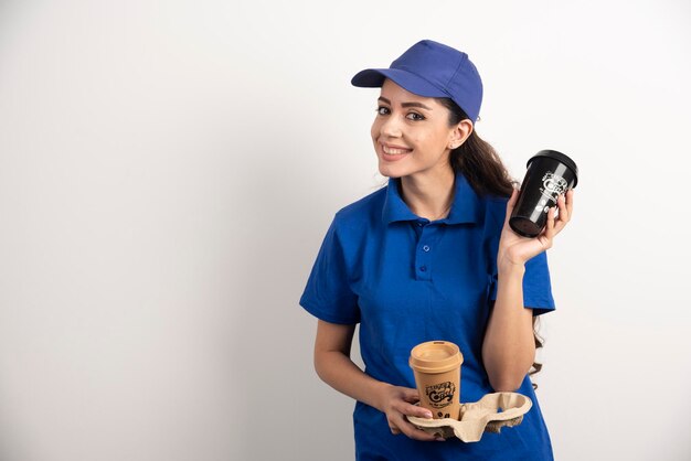 Улыбающаяся женщина-курьер с двумя чашками кофе. Фото высокого качества