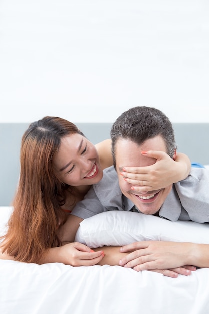 Smiling Woman Covering Husband Eyes in Bed