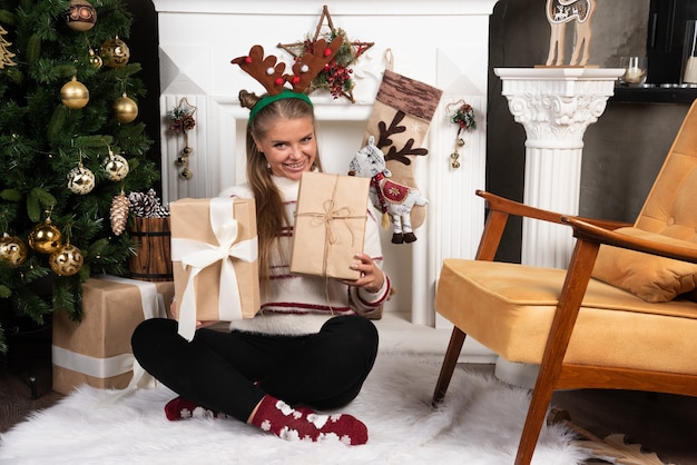 Smiling woman in deer ears holding two Christmas presents.