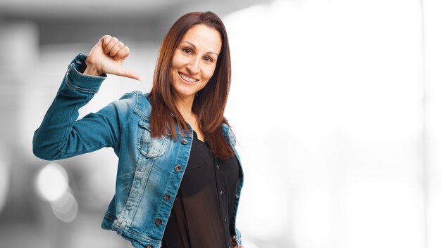 Smiling woman in denim jacket pointing at herself