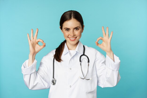 Smiling woman doctor professional medical worker showing okay ok sign in approval recommending clini...