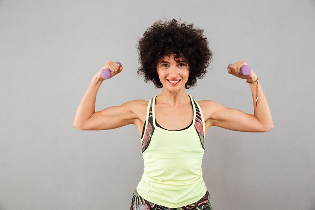 Smiling woman doing exercise with dumbbells and showing her biceps