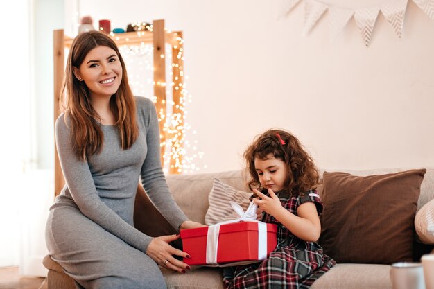 Smiling woman in dress giving gift to child. Little birthday girl posing with mother.