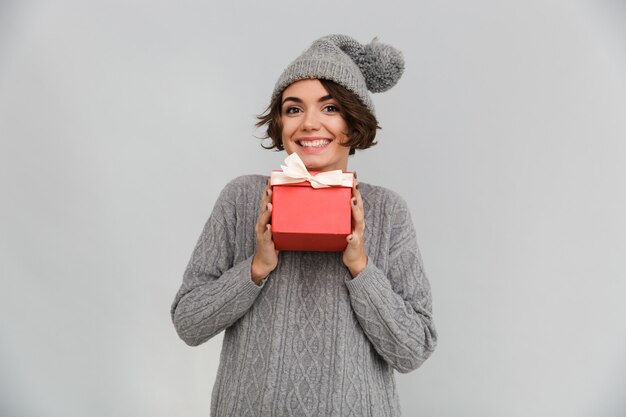 Улыбающиеся женщина, одетая в свитер и теплая шапка, держа подарок.