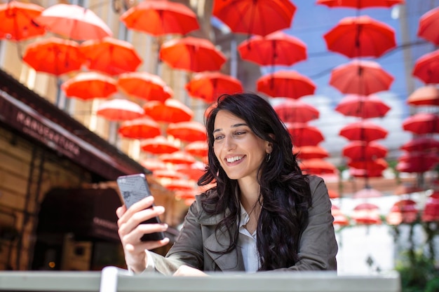 Foto gratuita donna sorridente che beve caffè e usa il suo telefono cellulare donna soddisfatta che gode della tazza di caffè ritratto ravvicinato di bella ragazza che beve caffè e fa un selfie