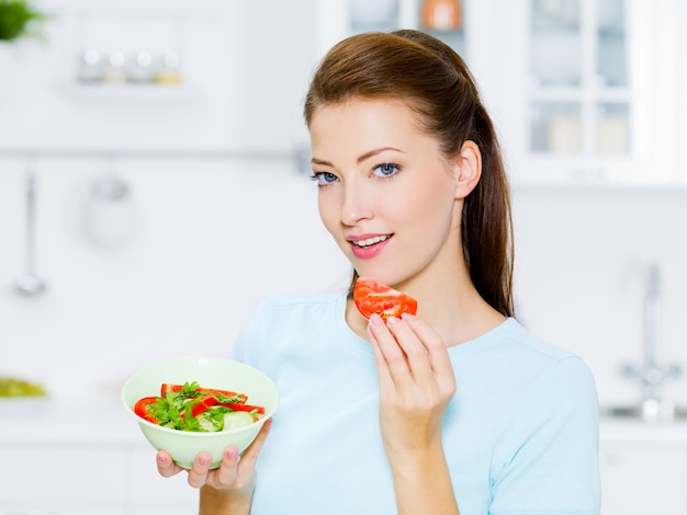 Foto gratuita la donna sorridente mangia la verdura in cucina