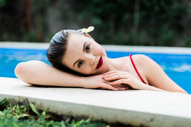 Улыбающаяся женщина на краю бассейна. Женщина в бикини, расслабляясь в бассейне в летний день.