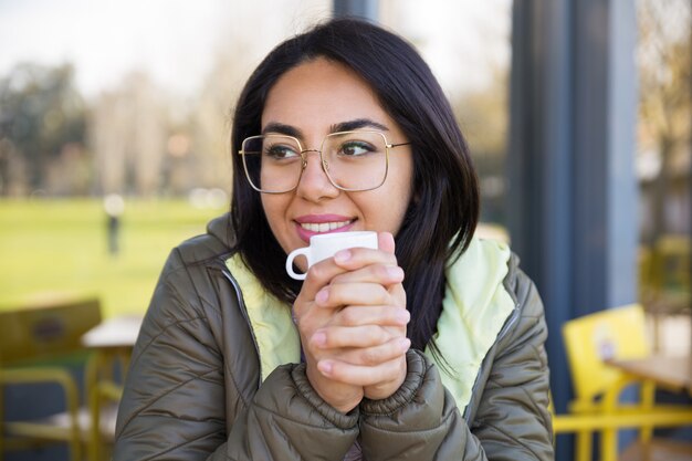 屋外カフェでホットコーヒーを飲みながら楽しんでいる笑顔の女性