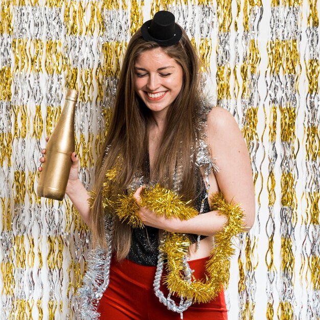 Smiling woman in evening wear with bottle of drink and tinsel 