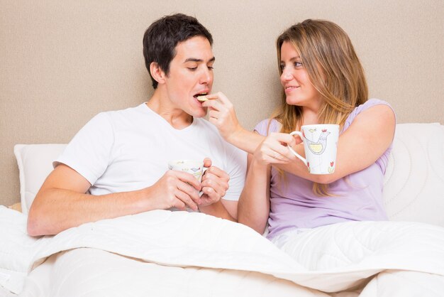침대에 앉아 그녀의 남자 친구에게 쿠키를 먹이 웃는 여자