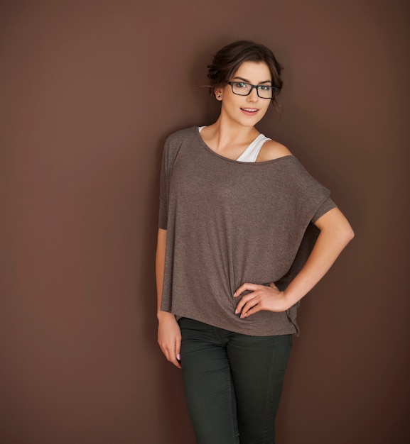 Free photo smiling woman in glasses posing on brown wall