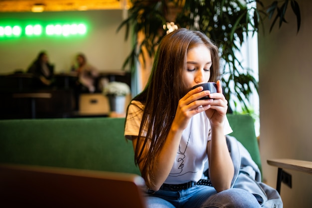 Donna sorridente di buon umore con la tazza di caffè che si siede nella caffetteria.