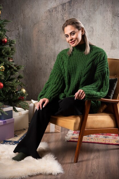 Smiling woman in green warm sweater sitting on the chair and posing 