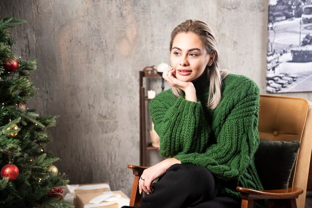 녹색 따뜻한 스웨터에 웃는 여자는 의자에 앉아 포즈