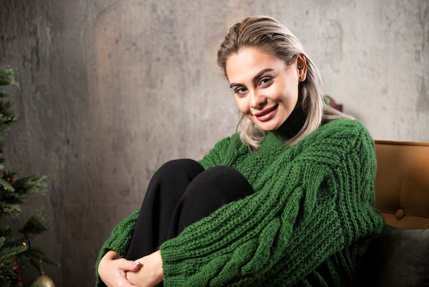 Donna sorridente in maglione caldo verde che si siede sulla sedia e in posa