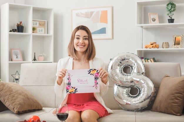 Smiling woman on happy women's day holding greeting card sitting on sofa in living room