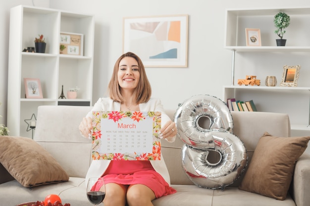 Smiling woman on happy women's day holding out calendar sitting on sofa in living room