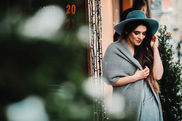 Smiling woman in hat and sweater stands in light dress on a winter street