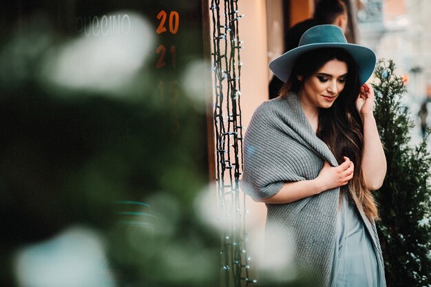 Smiling woman in hat and sweater stands in light dress on a winter street 