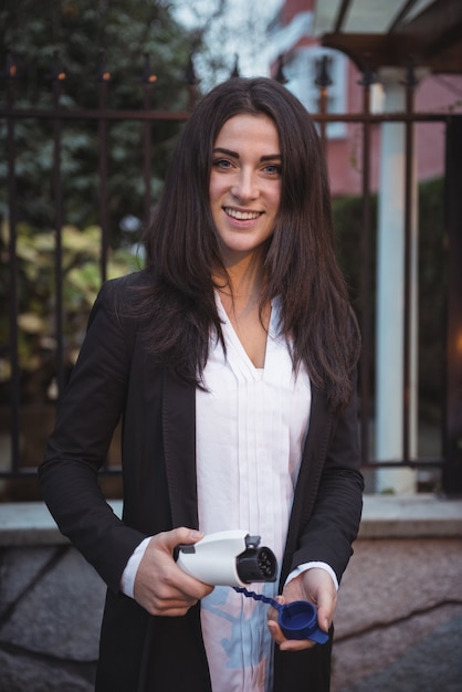 Free photo smiling woman holding car charger at electric vehicle charging station