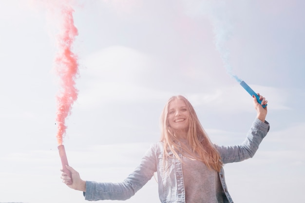 Free photo smiling woman holding colored smoke bombs