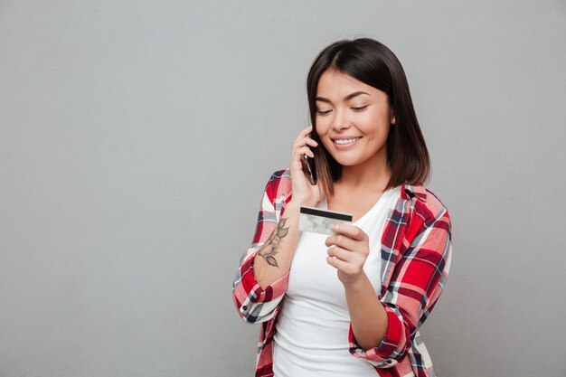 Smiling woman holding credit card and talking by mobile phone